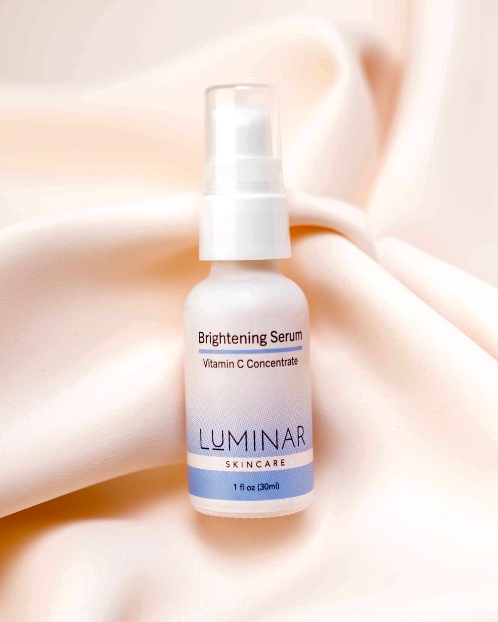 Luminar Brightening Serum bottle placed on neutral peach fabric, symbolizing skin illumination and even tone.
