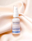 Luminar Brightening Serum bottle placed on neutral peach fabric, symbolizing skin illumination and even tone.
