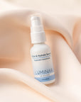 Luminar Glow & Hydrate Hyaluronic Serum bottle lying on soft peach fabric, highlighting deep hydration and radiance.
