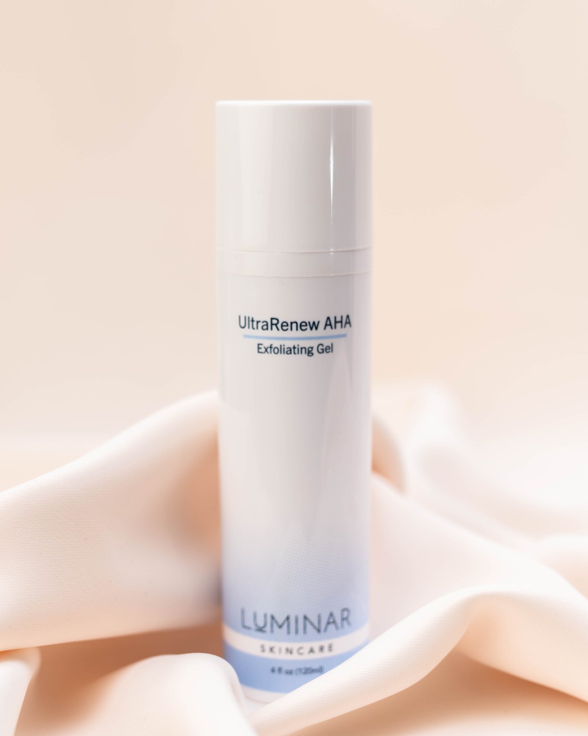 Luminar UltraRenew AHA Exfoliator Gel bottle on elegantly draped peach fabric, evoking gentle exfoliation and renewal.