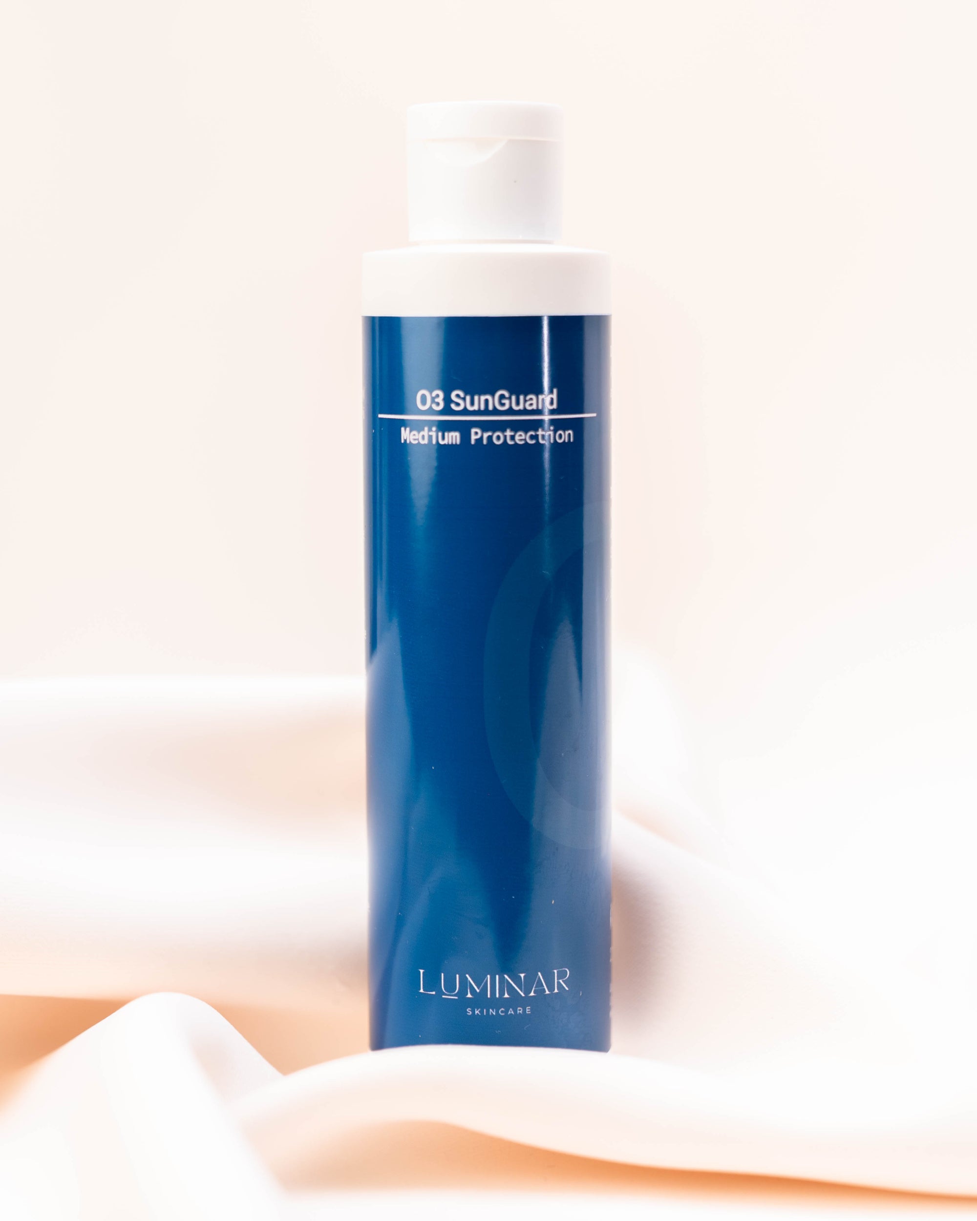 Luminar O3 Sunguard bottle placed on softly draped peach fabric, representing protective skincare.