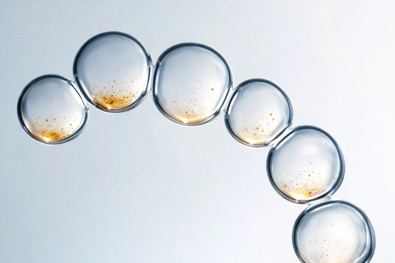 Clear skincare serum bubbles arranged in a curved line with visible golden coffee particles, representing the coffee-infused formula used in O3 Body Toning cream.