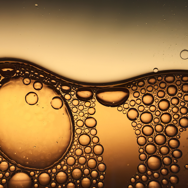 Abstract macro image of golden microbubbles in a nourishing liquid, representing oxygenated soothing oil.